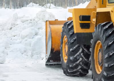 Heavy equipment vehicle clearing snow with a front-mounted plow on a snow-covered surface