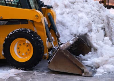 Skid-steer loader parked on a snow-covered surface beside a large pile of snow