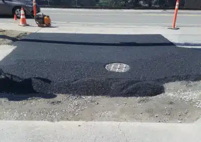 Fresh asphalt patch laid over a damaged street area near a curb with a manhole cover