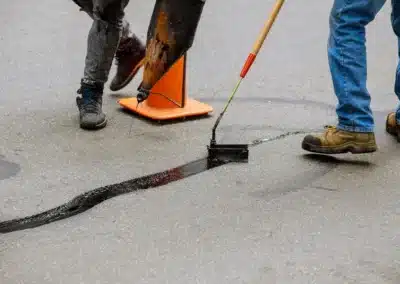 Workers applying crack fill sealant to a wet asphalt road