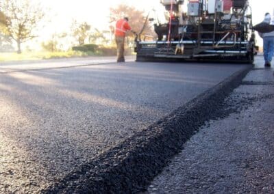 Paving machine laying down fresh asphalt on a road with workers nearby