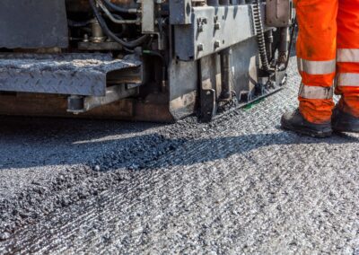 Close-up of heavy asphalt paving equipment at a construction site with fresh asphalt in front