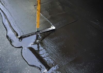 Squeegee applying seal coating to a dark asphalt surface